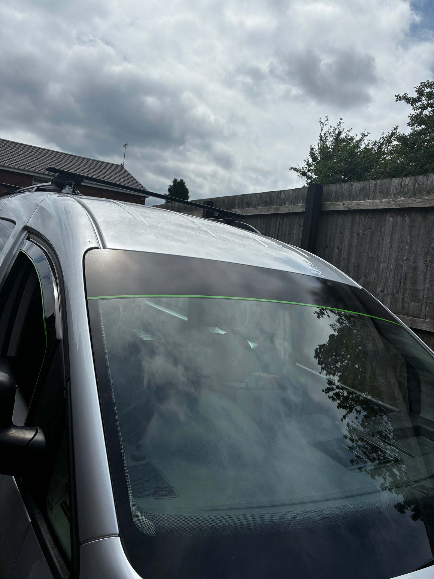 a silver car parked in a driveway, with a wooden fence and trees visible in the background.